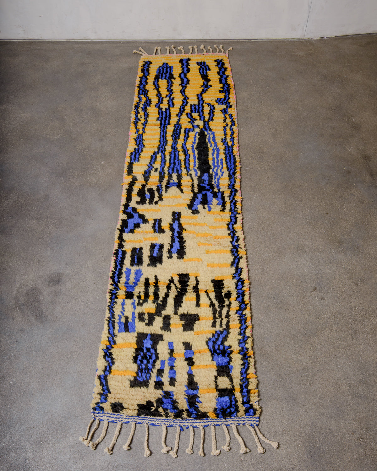 Vintage Berber runner rug made of colourful wool, laying on concrete floor.